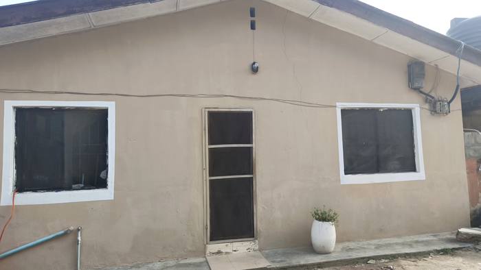 Front of Jadshion Hostel: a beige bungalow with a front door, two windows and a potted plant